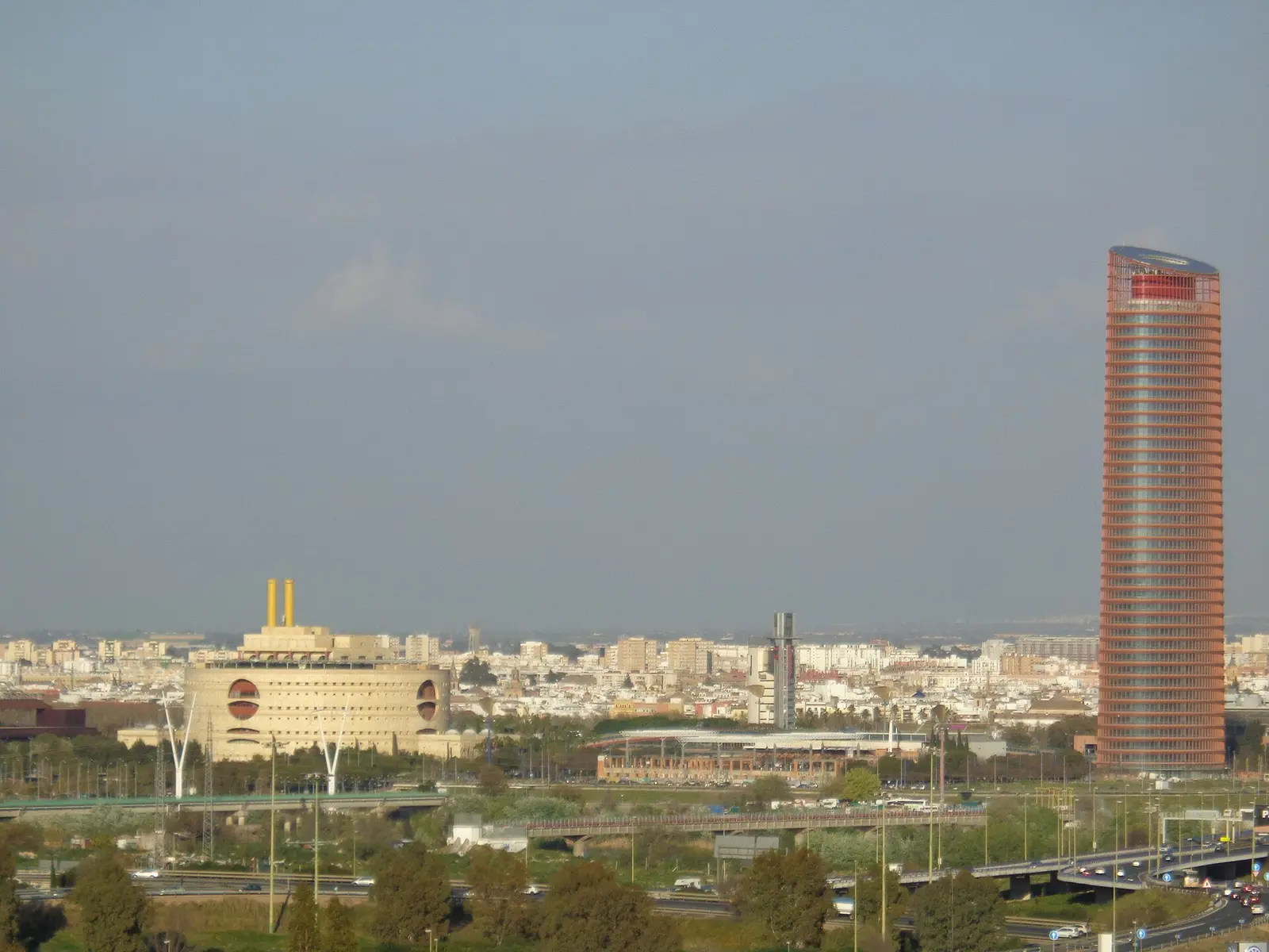 Vista desde Castilleja de la Cuesta hacia Sevilla, con la Torre Sevilla y el edificio circular de Torre Triana sobre la ciudad y, en primer término, autovías y pasos elevados