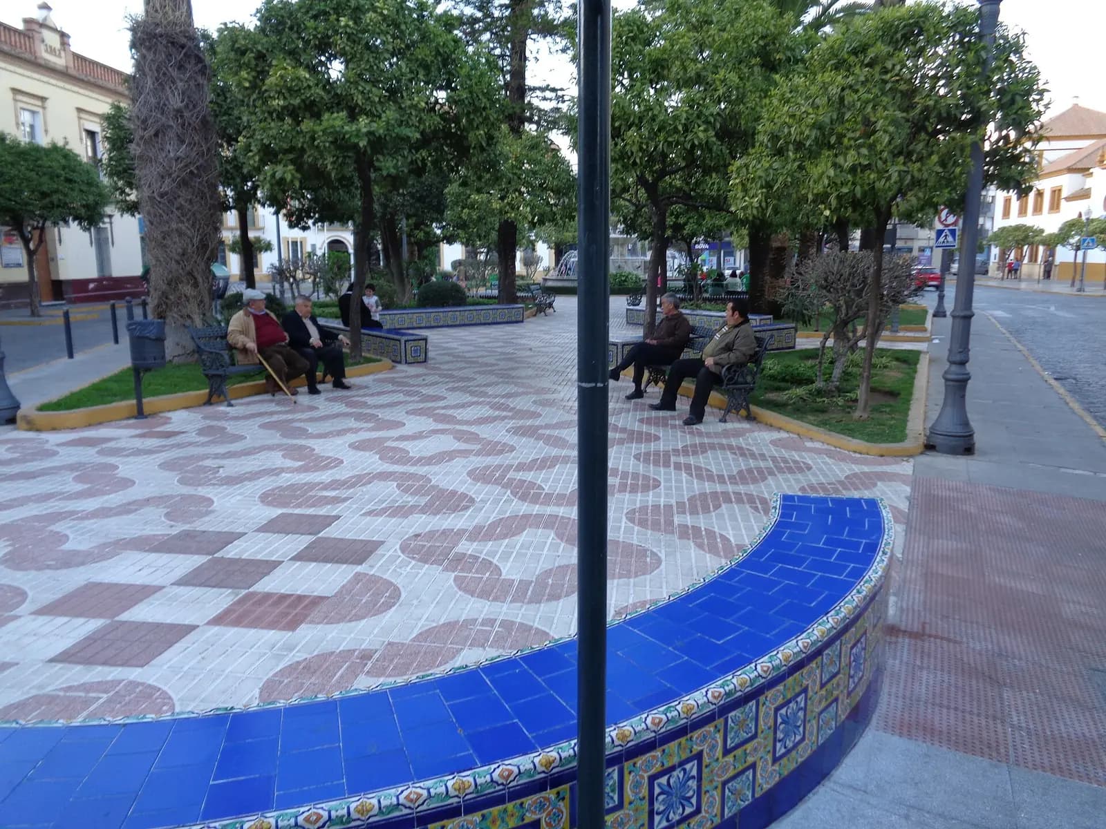 Plaza de la Constitución de Dos Hermanas con naranjos, bancos, solería de dibujo rojo y blanco y un banco corrido de azulejo azul en primer plano
