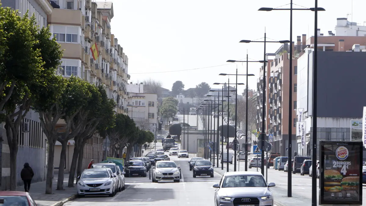 Avenida de Montequinto con bloques de pisos de ladrillo a la izquierda, farolas altas en la mediana, coches aparcados y edificios de varias plantas al fondo
