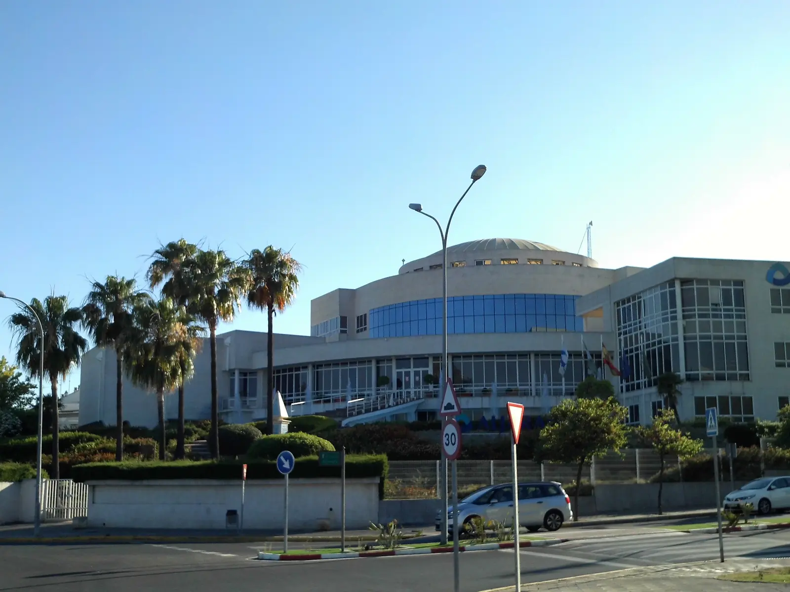 Edificio de la sede de Aljarafesa en Tomares, con fachada curva acristalada, cúpula baja y palmeras delante