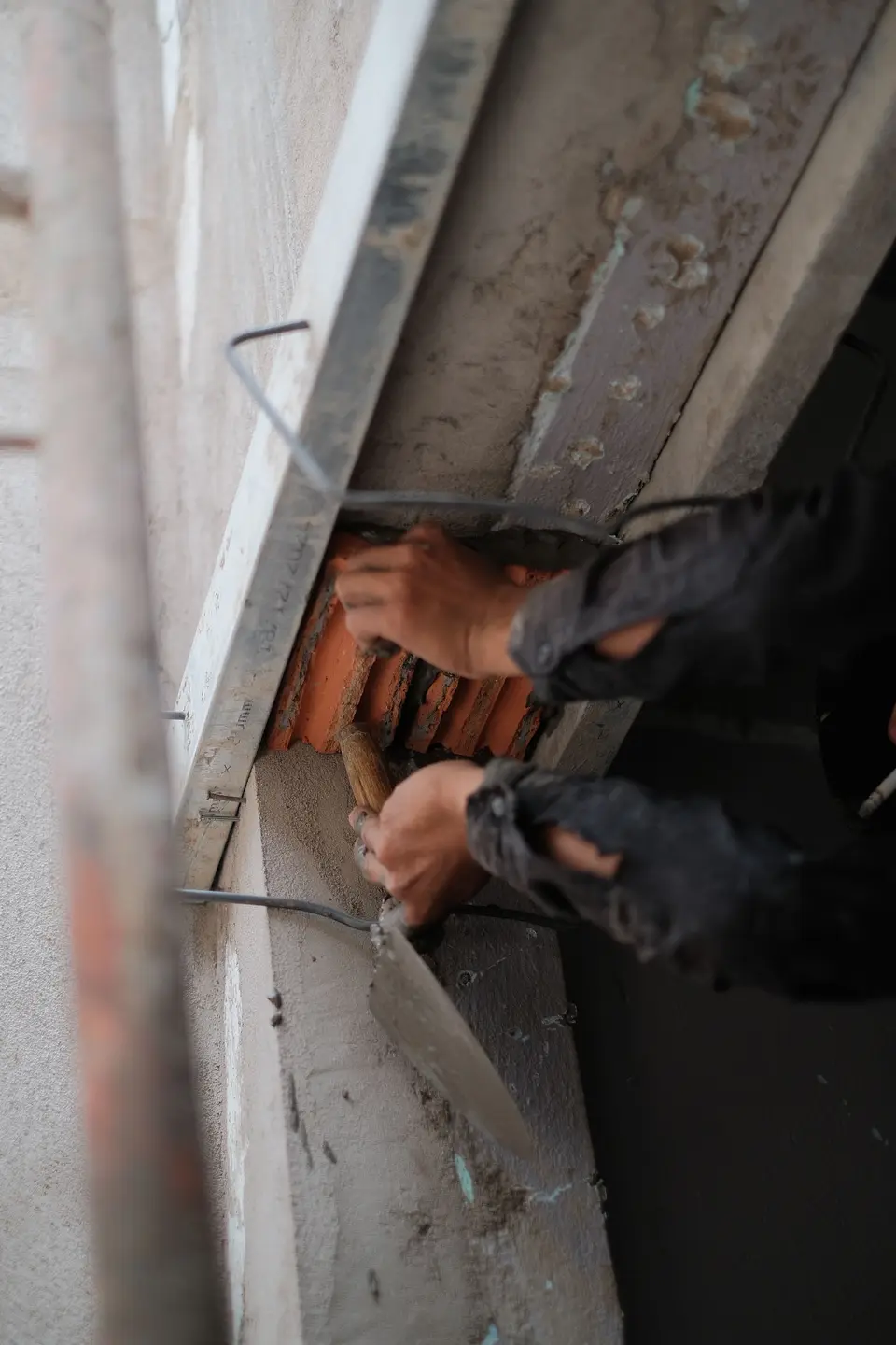 Manos con guantes trabajando el mortero con una llana junto a una pared